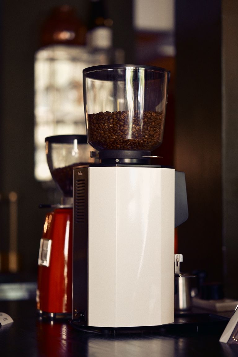 Sleek coffee grinder filled with beans in a warm-lit café, capturing the essence of coffee culture.