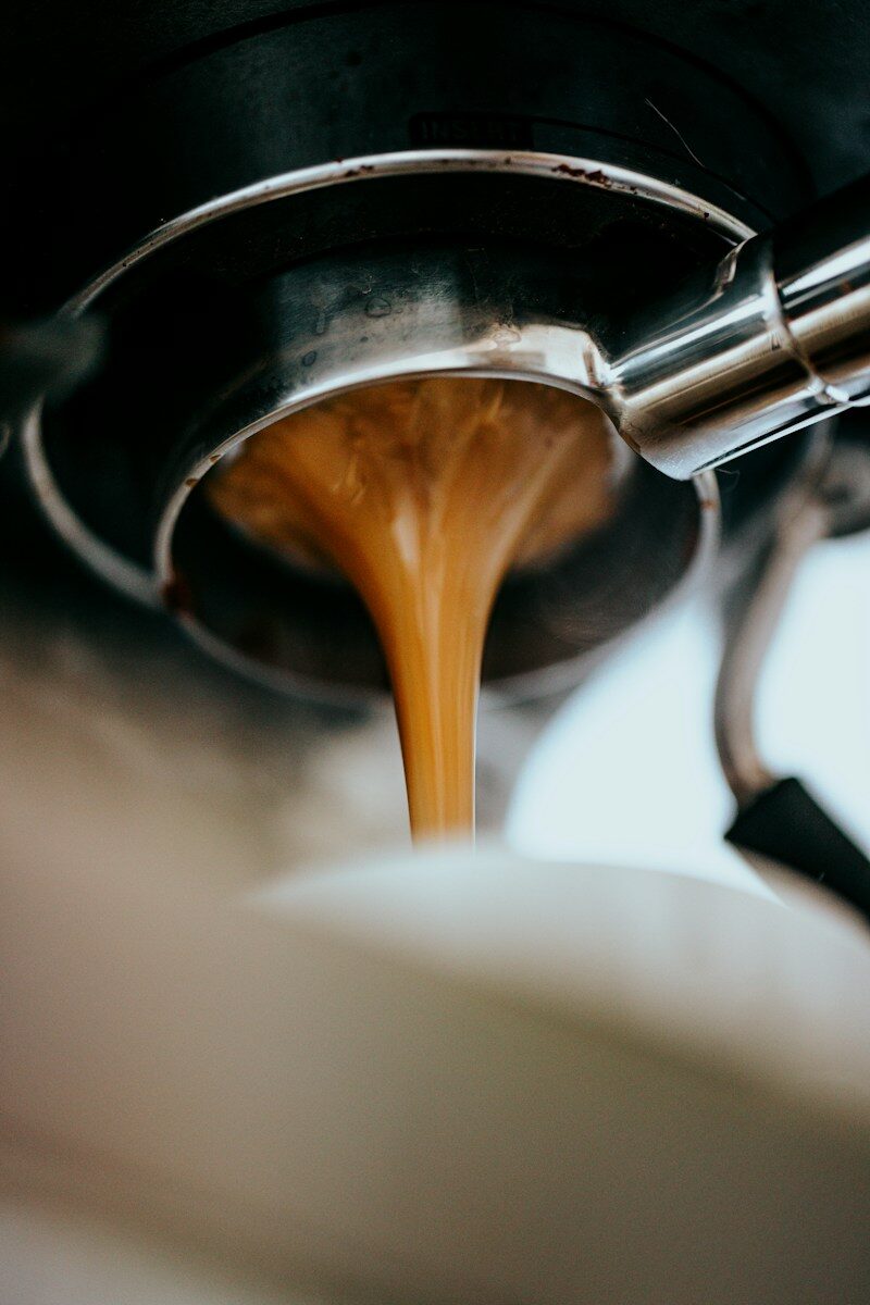 Espresso pouring from a metal portafilter into a white cup